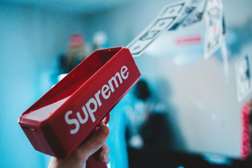 Close-up shot of a red toy gun labeled 'Supreme' shooting fake money, with a blurred background.